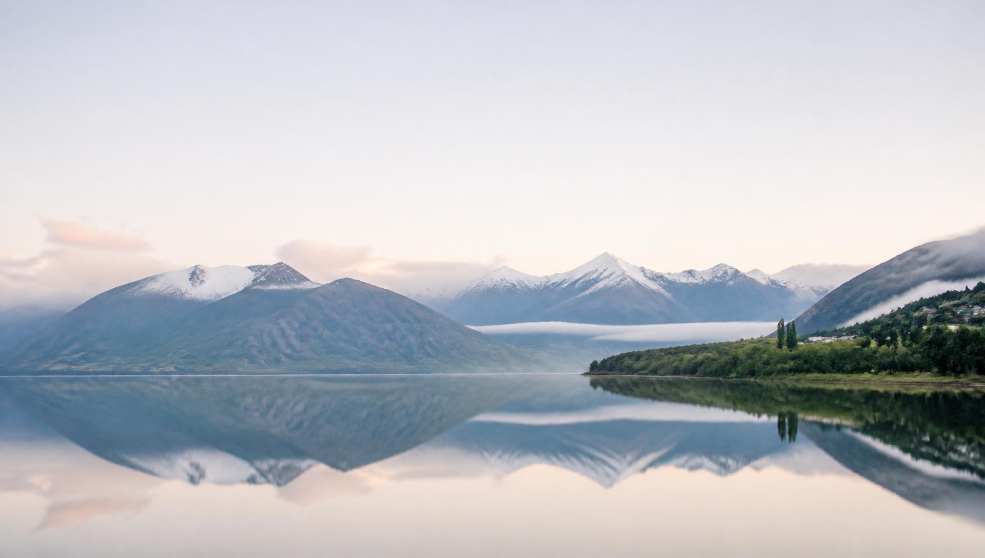 Still lake reflecting snow-capped New Zealand mountains at dawn